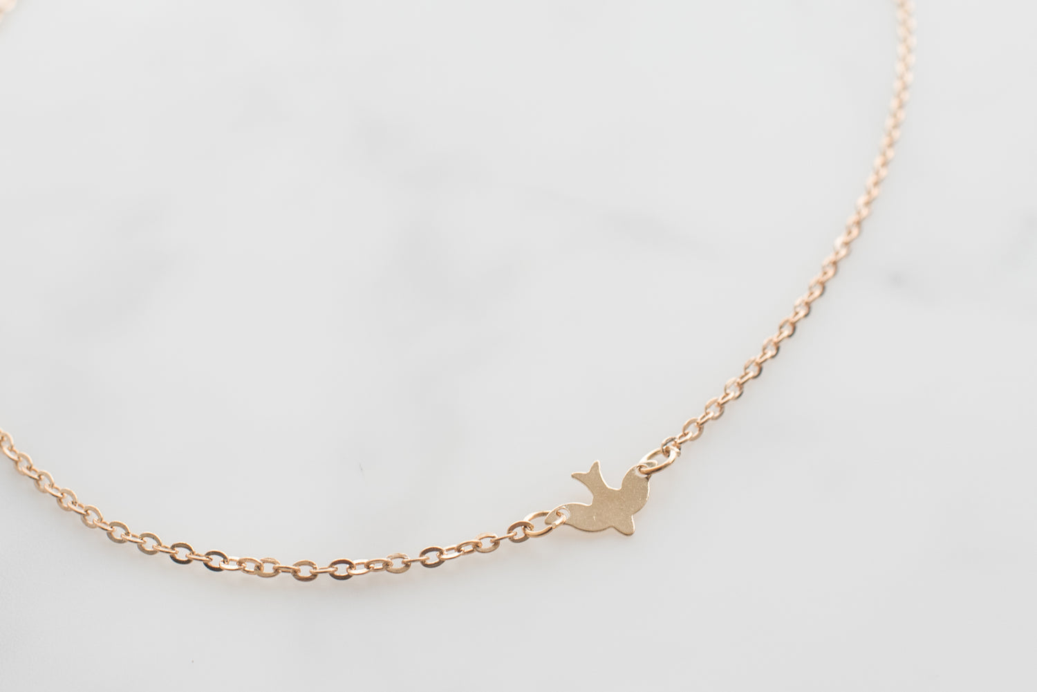 gold chain with a bird figure in the middle on a white marble table