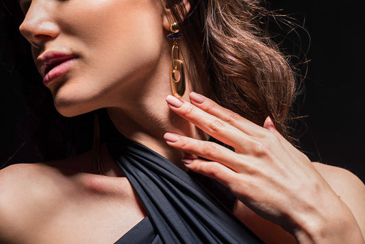 A close-up image of a woman's hand with manicured nails delicately touching a beautifully crafted earring.